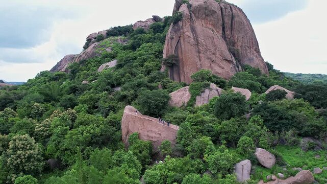 A cinematic aerial view of adventurers rappelling down a massive rock amidst the Ramanagara Hills