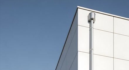 Obraz premium Modern Industrial Building Corner With Downspout Against Clear Blue Sky