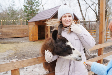 Woman interacts with a llama at an animal farm in winter © Maria