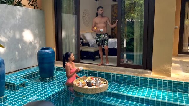 A couple enjoys a delightful breakfast in a private pool, surrounded by lush greenery. The charming setting creates a perfect holiday atmosphere in a luxurious villa, ideal for a romantic getaway.