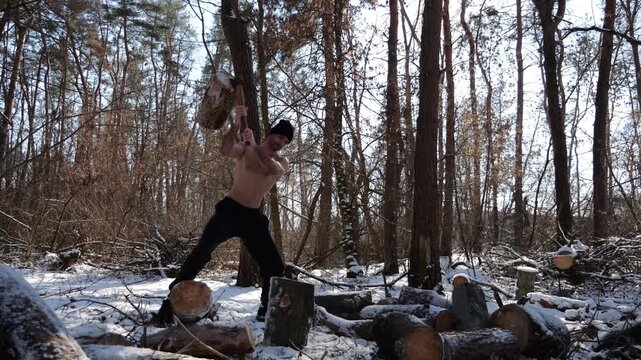 Shirtless young man chopping firewood in a sunny winter forest. Muscular guy working with axe in snowy woodland. Concept of strength, masculine, energy and harmony with nature during cold season