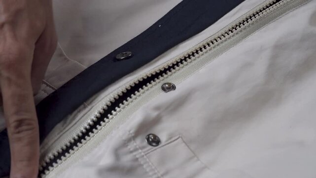 Close-up hand pulls a cream jacket zipper
