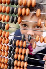 Little boy looking through colorful abacus beads, learning math at home or school, childhood education toy close up.