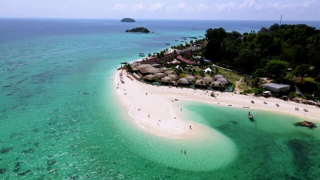 Breathtaking view of Koh Lipe Thailand stunning coastline, featuring soft white sand and vibrant turquoise waters. Visitors relax and enjoy various activities under a sunny sky.