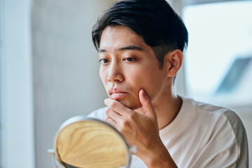 Asian young man checking his skin in mirror at home	
