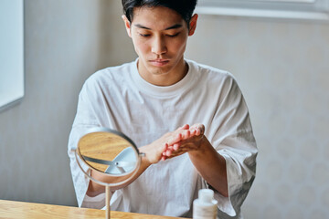 Asian young man applying skincare lotion in front of mirror