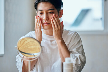 Asian young man applying skincare to forehead in front of mirror