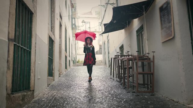 Stylish young woman with red umbrella walking in rain