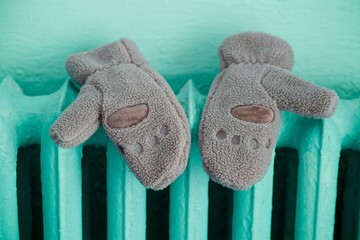 Two fluffy gloves hanging on a hot iron battery. Symbol of expensive heat supply tariffs, utility bills and keeping warm in a freezing apartment. Photo © slexp880
