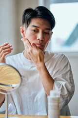 Asian young man applying skincare to forehead in front of mirror
