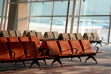 Sunlight streams across empty rows of orange and grey seats inside a modern airport departure lounge