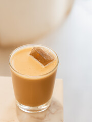 Minimalist iced latte in glass with coffee ice cube on marble table
