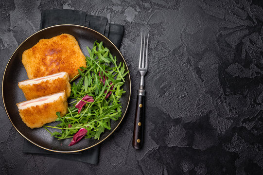 Chicken cordon bleu cutlet with cheese and ham on plate with salad. black background. top view