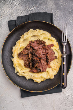 German Braised Beef Cheek, Slow cooked meat with smashed potatoes on a plate. grey background. top view