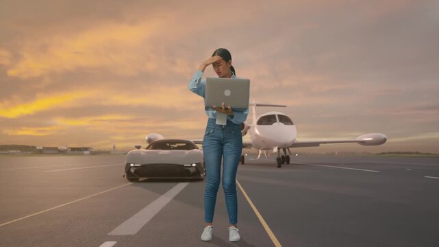 Full Body Of Asian Female With Her Laptop with Luxury Private Jet and Supercar on Airport Runway at Sunset, She Is Nodding Her Shead With Dissapionted