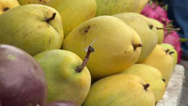 Yellow ripe mangoes are displayed for customers on a fruit stall, with colorful produce rows and active market trade behind. Ripe fruit sales.