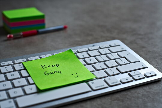 "Keep Going" green sticky note left on keyboard. The bright note stands out against the keys, symbolising motivation, productivity, and a focused mindset.