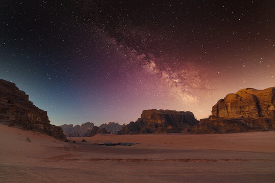 Milky way shines over red desert landscape with rocky formations at night. Wadi Rum, Jordan.