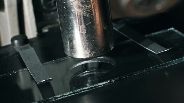 Close-up of a microscope lens over a glass concavity slide held by metal clips. A pipette adds a clear liquid drop for sample preparation in a scientific biology lab.