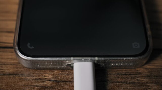 Macro shot of a phone charging as a USB-C cable connects with a blue electric arc visualization on screen. The device rests on a wood table indicating rapid power flow and energy.