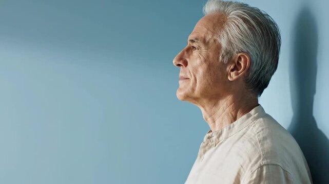 This video features an elderly man in a light-colored shirt, seen in profile against a soothing blue background. His consistent side-gaze and serene facial expressions evolve subtly, hinting at quiet