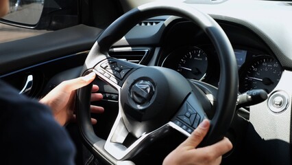 Male arms holds steering wheel while driving a motor car at city. Young man operating the automobile at urban road. Driver moving in his auto on route. Slow motion