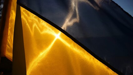 Blue-yellow symbol of Ukraine waving at wind against the background of sunlight. Ukrainian flag illuminated by sun fluttering at countryside. Concept of peace and support against russian aggression
