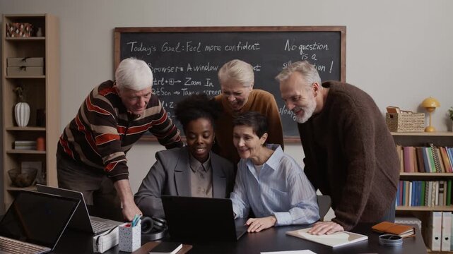 Caucasian senior students collaborating with Black female teacher while using laptop in classroom focused on digital education
