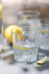 Close-up of a faceted glass filled with lemon water placed on a gray table, with a lemon wedge nearby and soft natural lighting