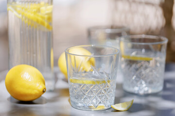 Outdoor setup of lemon water in crystal glasses and glass pitcher, with lemons and shadows creating a calm, refreshing mood