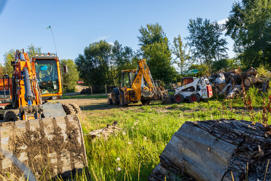 Heavy machines are working on a site with logs and green grass under a clear sky in a rural setting during the day. Lutsk, Ukraine &ndash; August 27, 2025