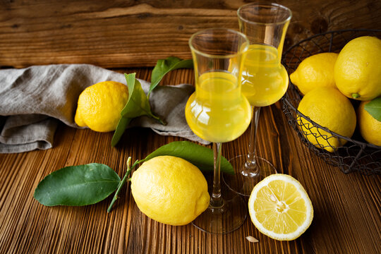 Limoncello in two glasses with ripe lemons on a rustic wooden base. Italian liqueur.