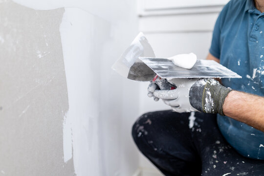 Worker applying finishing touches to drywall in a home renovation project during the day in a living room