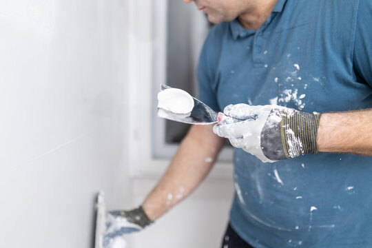 Worker applies wall plaster with a spatula in a room during home improvement project