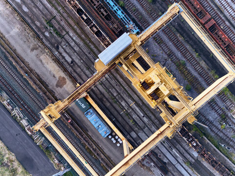 Irun, Spain - 22 November 2025: Aerial view of a colossal yellow crane standing guard over a yard filled with railway tracks and colorful train cars.