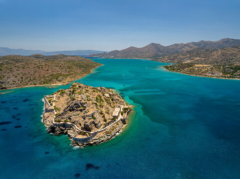 Aerial view of the ancient fortress island of Spinalonga stands resilient against the turquoise sea, a stark contrast to the rugged mountains, Spinalonga, Lasithi, Greece.