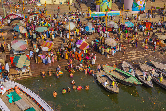 Aerial view of a bustling scene unfolds with boats lining the ghats as people gather for rituals along the Ganges River, Varanasi, Uttar Pradesh, India.