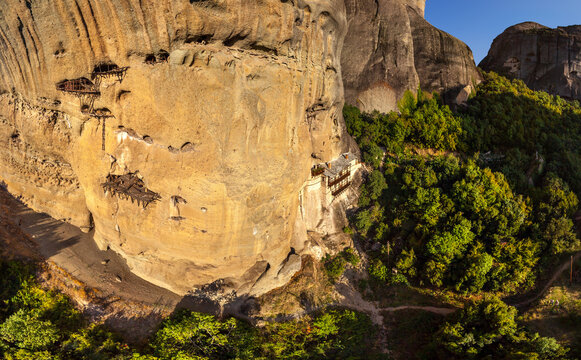 Aerial view of monasteries clinging to the towering cliffs, a blend of nature and architecture, bathed in the warm glow of the sun, Kalabaka, Trikala, Greece.