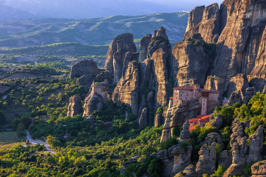 Aerial view of monasteries perched atop towering rock formations, bathed in the warm glow of the setting sun, Kalabak, Trikala, Greece.