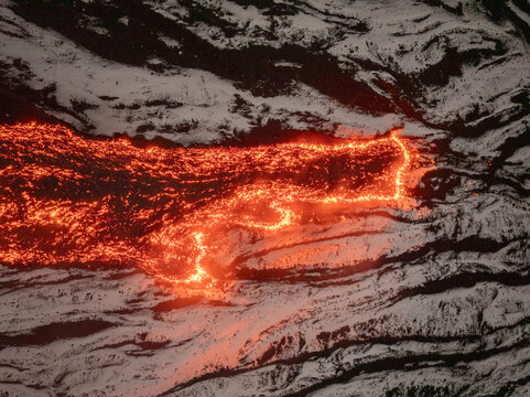 Aerial view of molten lava snaking through the dark, volcanic landscape, a fiery river cutting a path through the rugged terrain, Catania, Sicily, Italy.