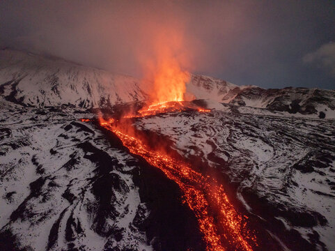 Aerial view of fiery lava flows dramatically cutting through the stark white snow-covered landscape of Mount Etna, a mesmerizing clash of elements, Catania, Sicily, Italy.
