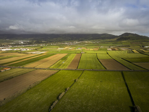 Aerial view of vibrant patchwork fields stretch towards the horizon beneath a brooding sky, Santa Barbara, Azores, Portugal.