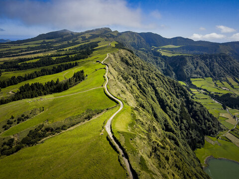 Aerial view of a winding road snakes along the vibrant green ridge, contrasting with the deep blue lake below, Sintra, Lisboa, Portugal.
