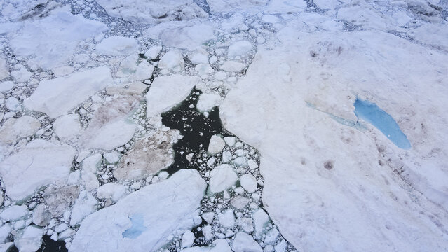 Aerial view of a stark, icy expanse is punctuated by pools of brilliant turquoise, contrasting against the monochrome landscape, Greenland, Greenland.