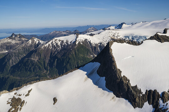 Aerial view of snow-capped peaks contrasting with deep green valleys under a vast blue sky, a sublime tapestry of nature's grandeur, Sitka, Alaska, United States.