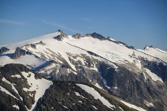 Aerial view of stark white snowfields contrast with the rugged, dark peaks under a clear sky, creating a dramatic alpine landscape, Sitka, Alaska, United States.