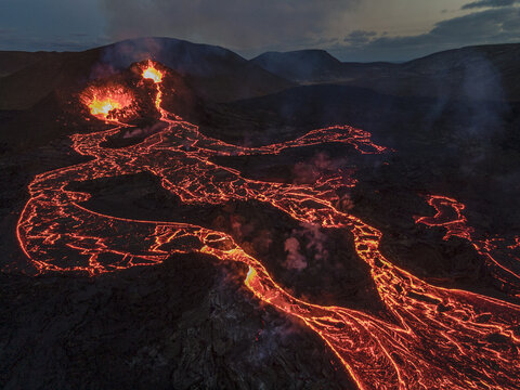 Aerial view of molten lava flowing through the dark volcanic landscape, a fiery river carving its path near Grindavik, Grindavikurbaer, Iceland.
