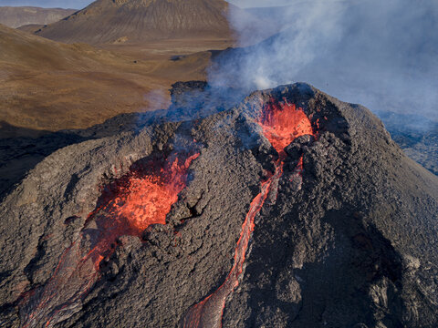 Aerial view of rivers of molten lava cascading down the rugged slopes of a volcanic mountain, creating a mesmerizing spectacle of fiery hues against the dark, textured terrain, Grindavik, Iceland.