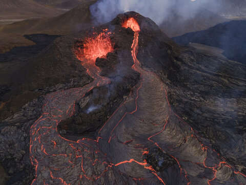 Aerial view of molten lava flowing like fiery rivers from a volcanic peak, contrasting against the dark, rugged landscape, Grindavik, Grindavikurbaer, Iceland.