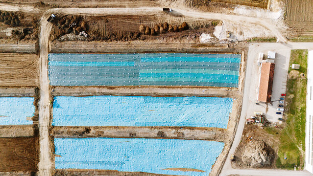 Aerial view of the geometric patterns of fields under blue plastic sheets and a terracotta-roofed building, creating a stark contrast, Sremska Mitrovica, Vojvodina, Serbia.